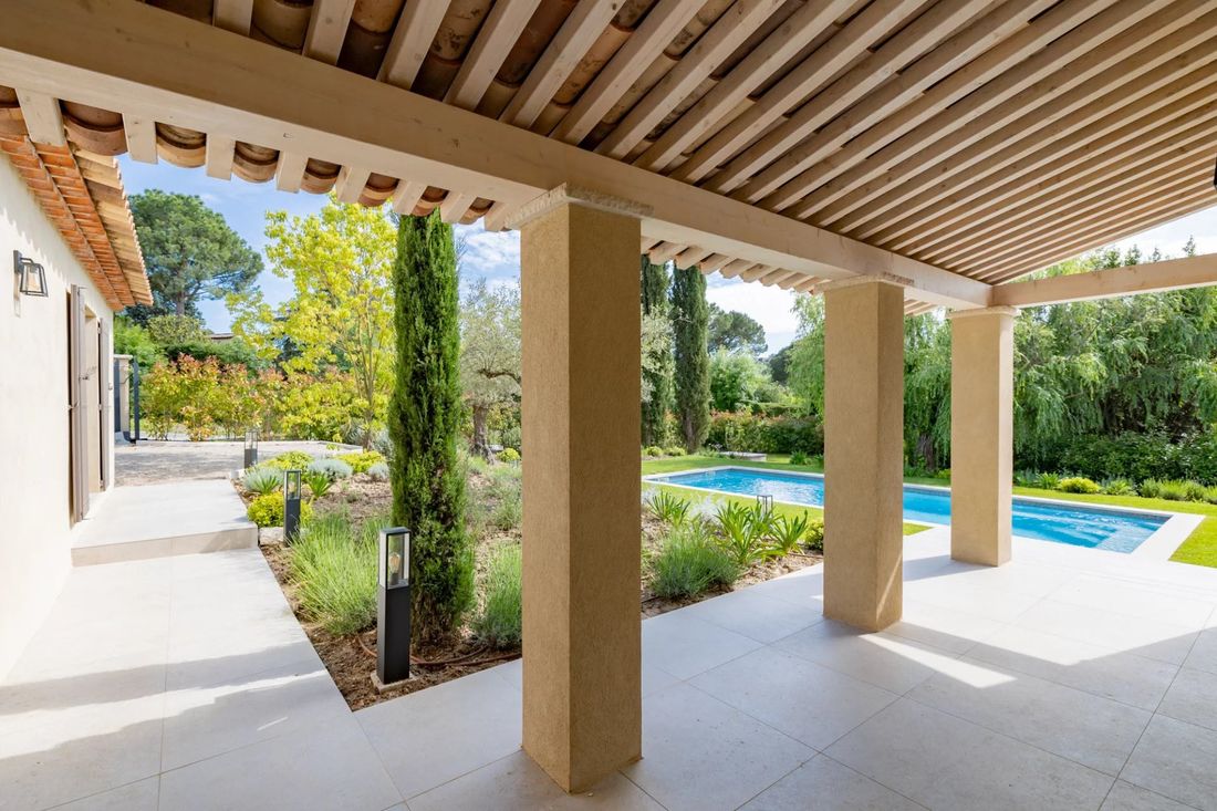 Terrasse couverte sous une pergola en bois, ouverte sur la piscine